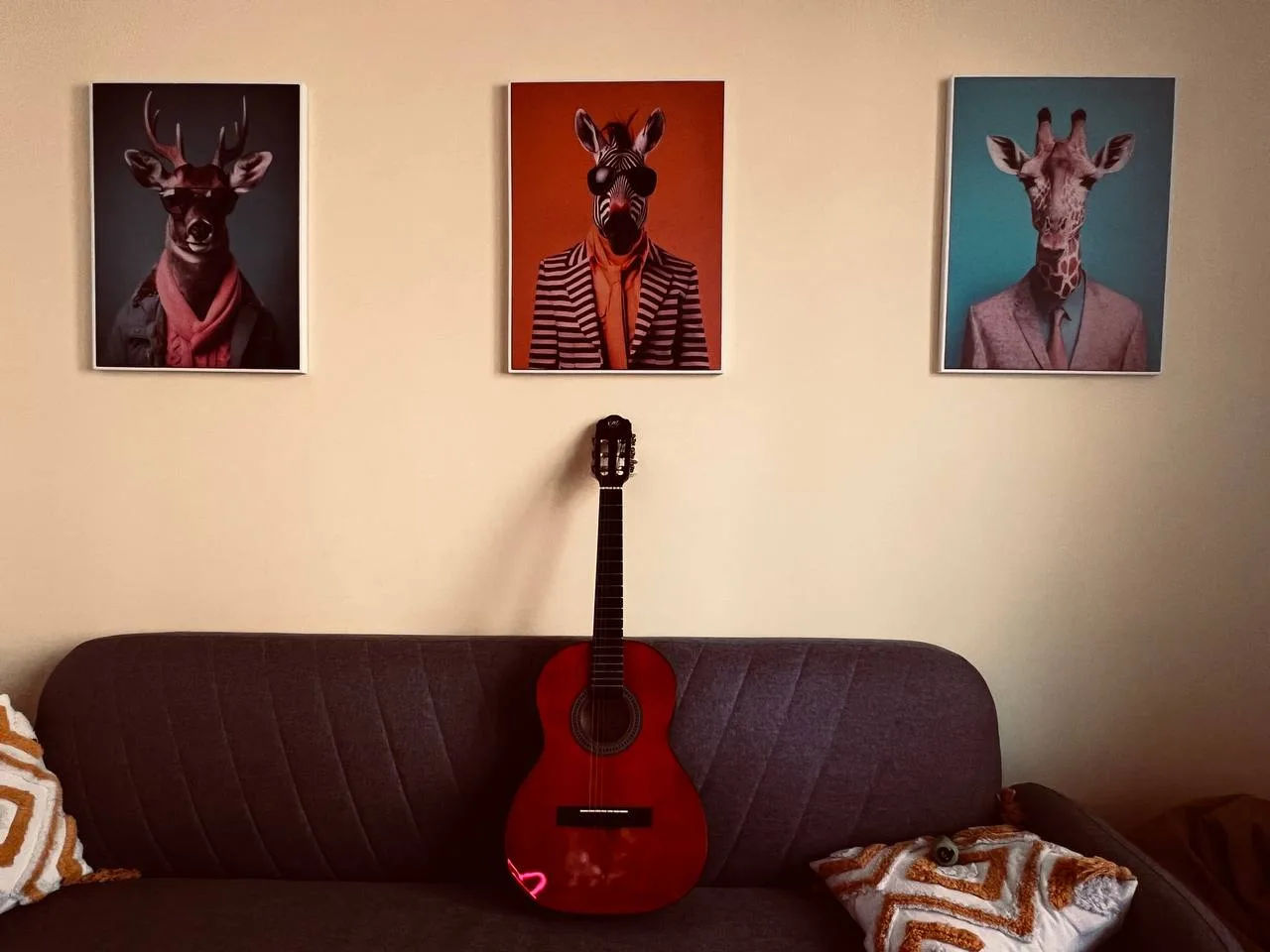 A guitar on a sofa beneath three framed animal portraits in the Codeburg lounge